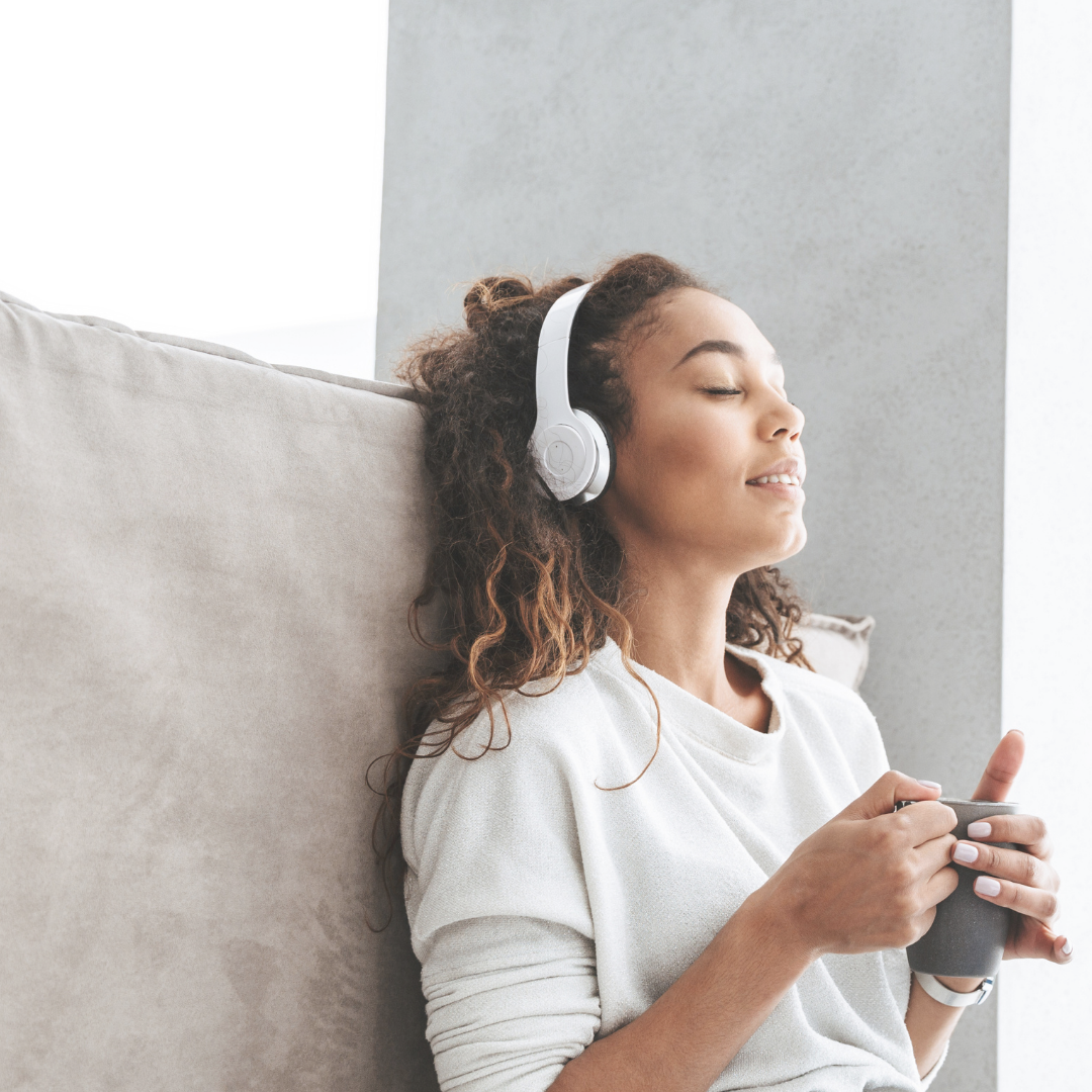NICU Mom woman of color with white headphones leaning against wall, listening to NICU Music Playlist