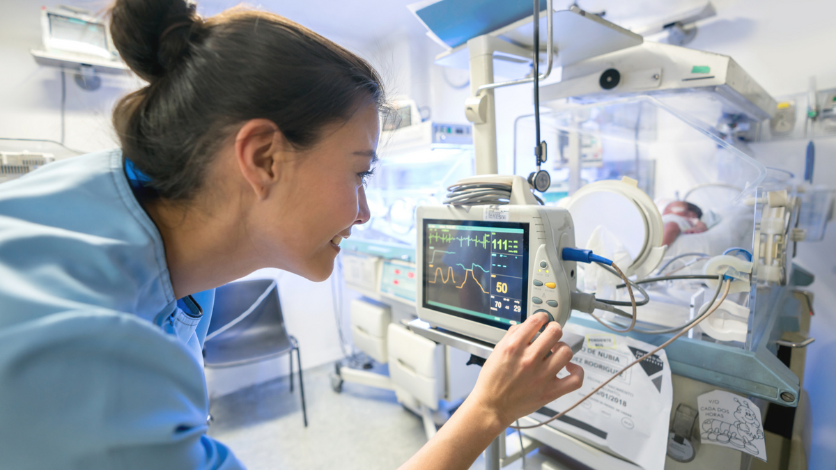 Nurse in NICU in blue scrubs by preemie baby in isolette